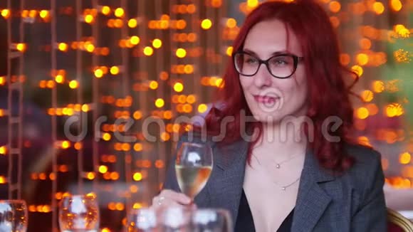 一个红头发的女人坐在餐厅的餐桌旁喝着香槟视频的预览图