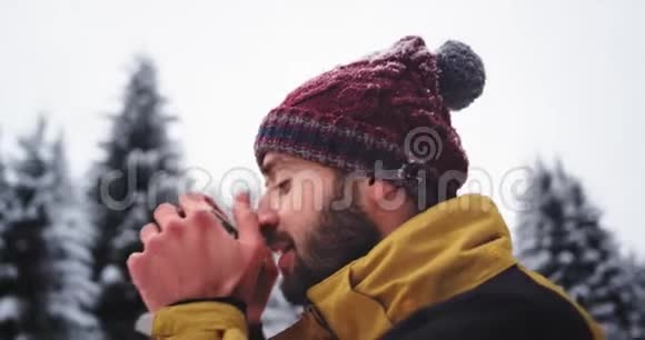 一个人在寒冷的冬天在雪林中喝热茶的肖像他欣赏周围的风景视频的预览图