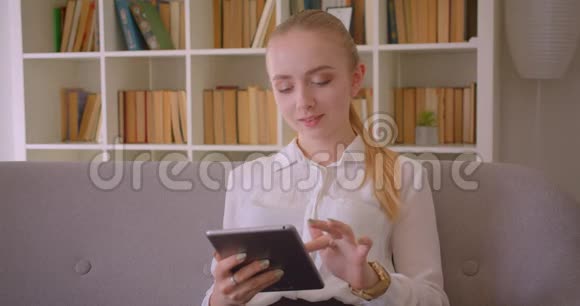年轻漂亮的白种人金发女学生用平板电脑看着镜头开心地笑着的特写照片视频的预览图