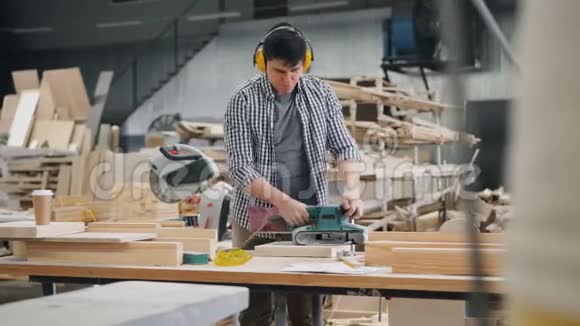 使用砂光带抛光机加工木材的防护耳机工人视频的预览图