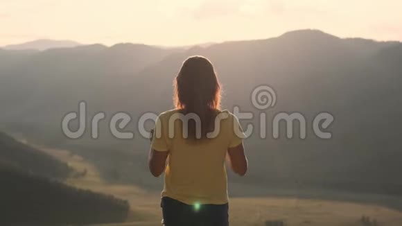 日落时分一位年轻女子来到悬崖边举起双手站在高高的岩石山前视频的预览图