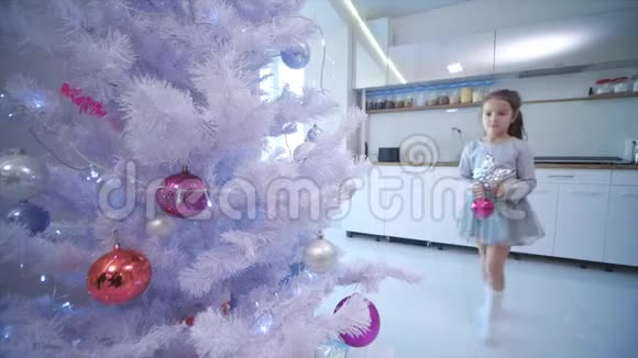 一个棕色小女孩在家里的一棵人造圣诞树上挂着一个粉红色的玻璃宝视频的预览图
