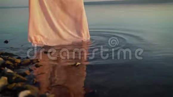 一个穿裙子的年轻女孩在水上散步日落时分美丽的女人在海边散步穿着视频的预览图