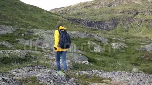穿着一件亮黄色夹克的女子背包客在山上散步视频的预览图