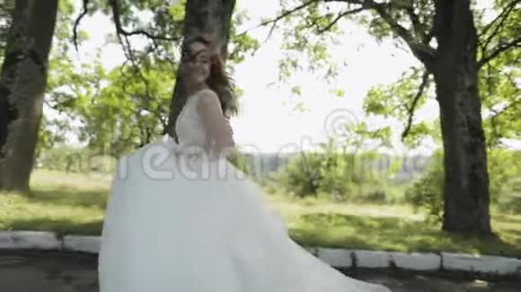美丽可爱的新娘穿着婚纱在公园里奔跑慢动作视频的预览图