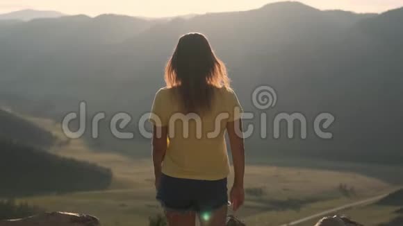 日落时分一位年轻女子来到悬崖边举起双手站在高高的岩石山前视频的预览图