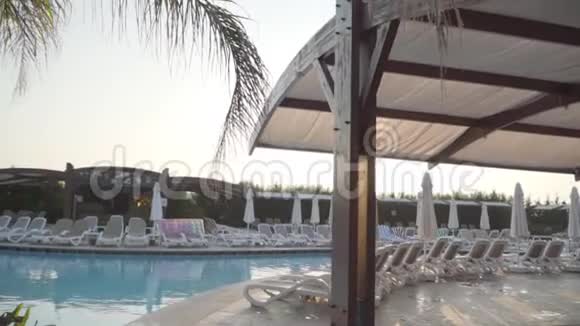 阳光照耀着游泳池清澈的水一排排白色的日光浴床沿着游泳池平静的手段视频的预览图
