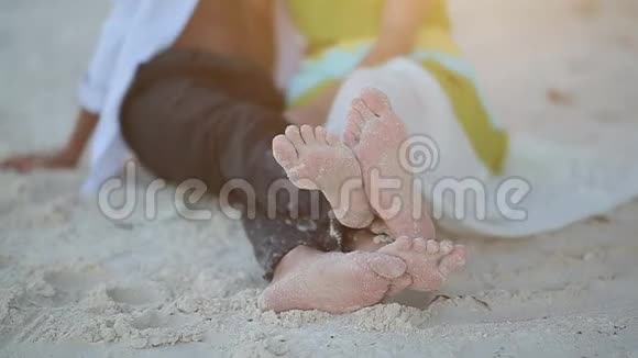 爱的夫妇躺在沙滩上赤着脚喜欢脚的游戏夕阳的光芒在镜框中滑落视频的预览图