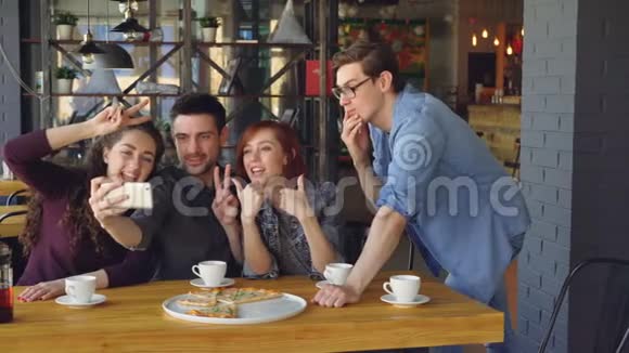 情绪化的年轻人正在现代咖啡馆里用智能手机摆姿势和大笑自拍现代科技有趣视频的预览图