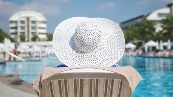 优雅的女士白帽在豪华酒店度假胜地的躺椅上放松欣赏游泳池视频的预览图