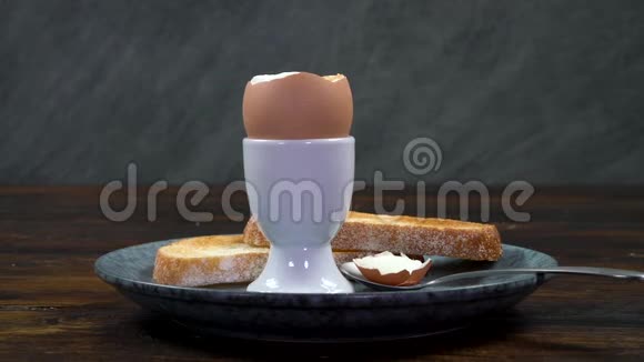 在木桌上的盘子里把一个土司士兵放进一个煮鸡蛋里视频的预览图