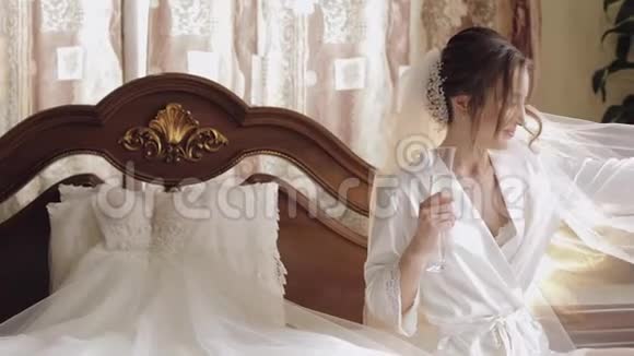 美丽可爱的新娘身穿睡衣头纱坐着喝香槟视频的预览图