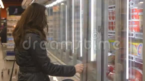 在超市买牛奶或冷藏食品的年轻女子在冷藏区打开冰箱的玻璃门视频的预览图