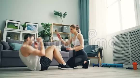年轻女孩和男孩做运动在家练习仰卧起坐拍手视频的预览图
