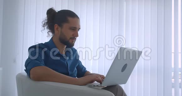 现代自由职业者在笔记本电脑上打字坐在光办公室的扶手椅上转向相机和手表视频的预览图