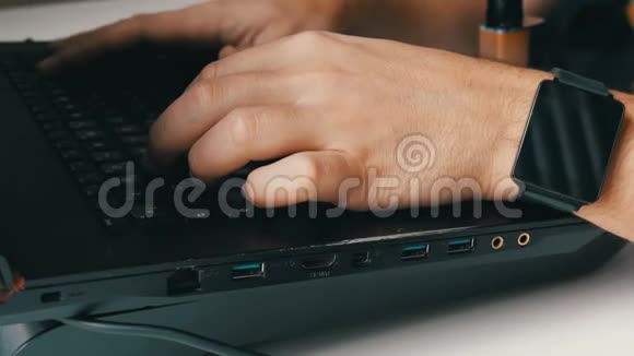 一个人在笔记本电脑上工作男人手里拿着一只智能手表和一支电子香烟在键盘上打字视频的预览图