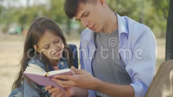 弟弟和妹妹在阳光明媚的秋日公园里坐在户外看书的画像视频的预览图