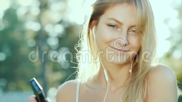 快乐的女人戴着耳机听音乐使用智能手机太阳美丽地照亮了她的头发视频的预览图