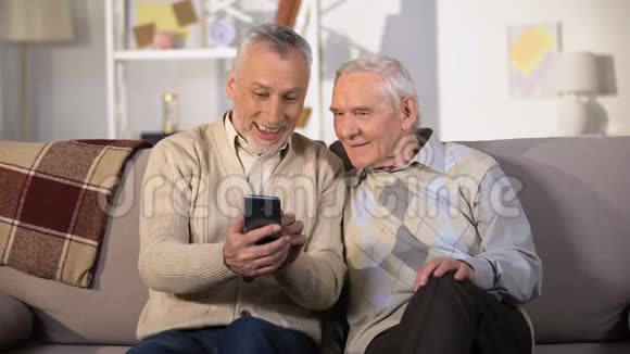 老年男子在智能手机上展示有趣的照片老年朋友在家玩得很开心视频的预览图