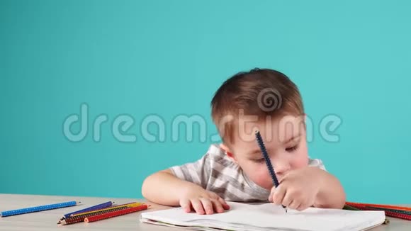 年轻有才华的男孩在蓝色背景的相册里画了一幅铅笔画视频的预览图