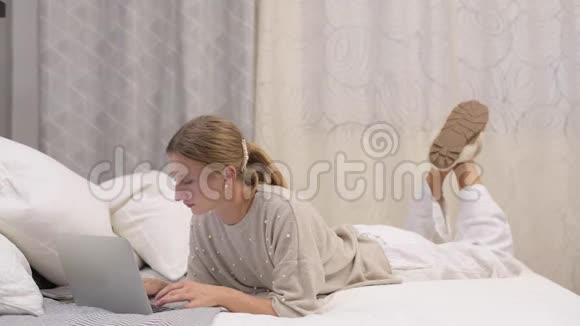 漂亮的女人正在床上的笔记本电脑上打字女子网上购物视频的预览图
