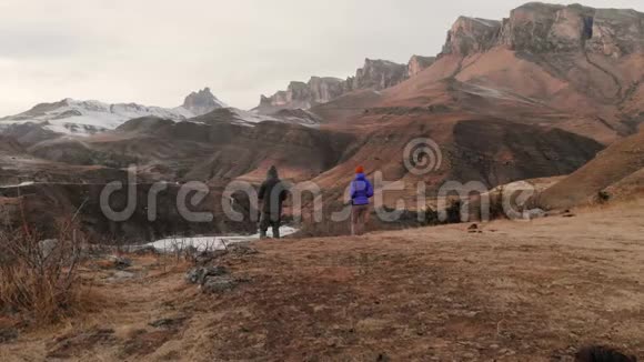 一对年轻夫妇站在靠近山湖的悬崖边上以史诗般的岩石为背景的鸟瞰图视频的预览图