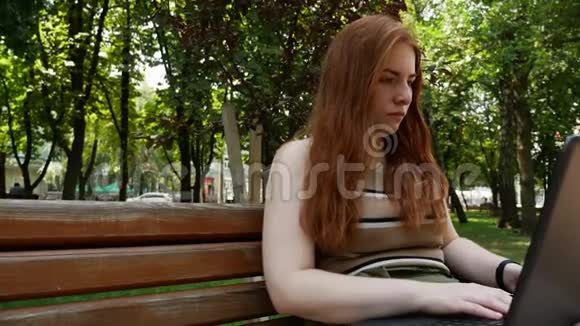 红发女孩在公园的笔记本电脑后面工作视频的预览图