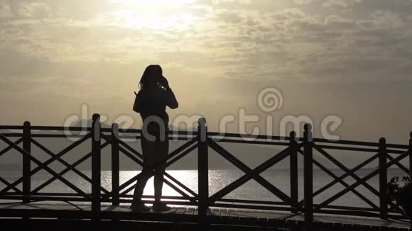 日落时分女孩在海边欢快地打电话动作缓慢视频的预览图