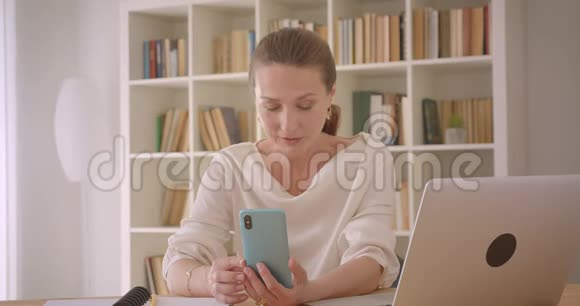 用手提电脑拍摄的白种人深色头发的老女商人的特写照片并在手机上播放视频视频的预览图