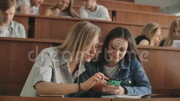 漂亮的女学生正在使用智能手机看屏幕有说有笑坐在大学的桌子上社会视频的预览图