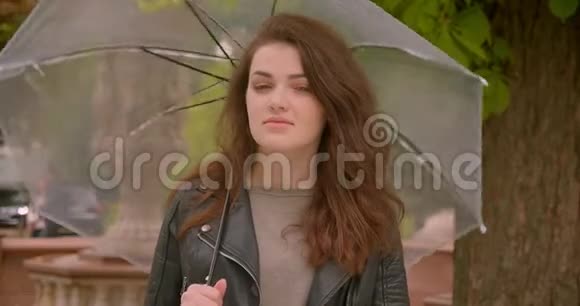 白种人黑发模特可爱的肖像在绿色公园里旋转着雨伞诱人地看着镜头视频的预览图