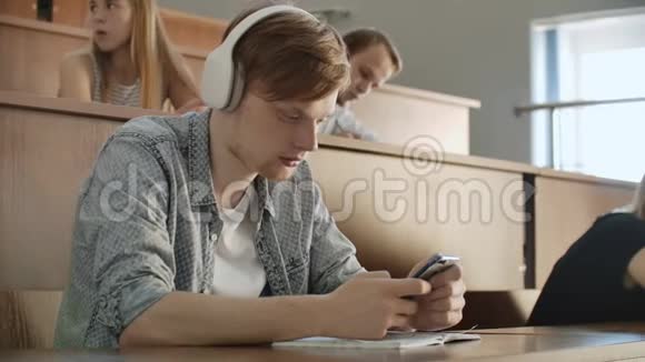 一个学生坐在大学礼堂里一大群人坐在耳机里听音乐和音乐视频的预览图