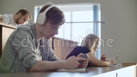 一个学生坐在大学礼堂里一大群人坐在耳机里听音乐和音乐视频的预览图