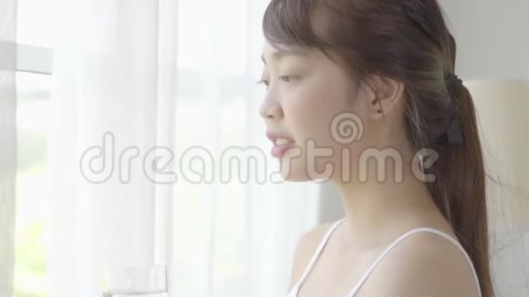 美丽的年轻亚洲女人醒来在家里喝着一杯水窗户是新鲜的视频的预览图