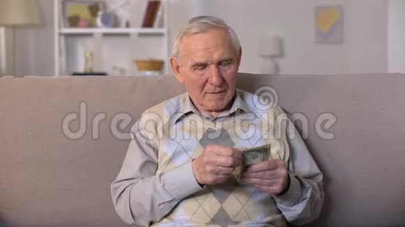 沮丧的老人坐在沙发上拿着钞票社会不安全视频的预览图