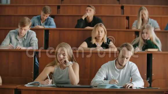 现代学生男人和女人坐在一个大教室的课桌前写一篇讲稿视频的预览图