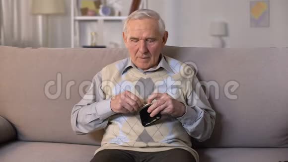 悲伤的老人坐在沙发上镜头前拿出空钱包贫穷视频的预览图