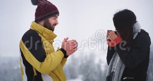 好朋友在白雪皑皑的森林中漫步在冰冻的日子里喝点热饮料取暖视频的预览图