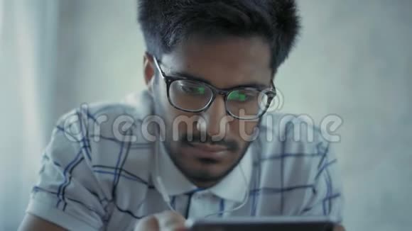 特写戴眼镜的印度学生戴着耳机躺在床上听音乐视频的预览图
