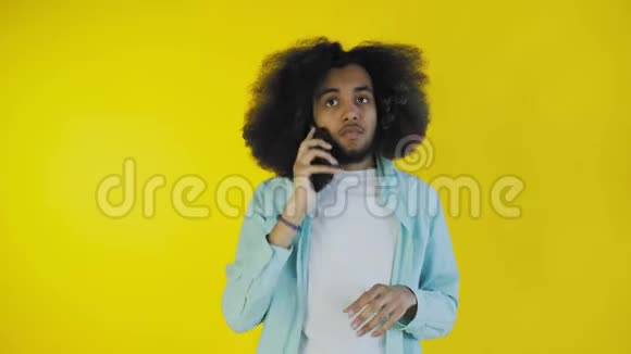 美国黑人男子在手机上交谈而站在黄色背景的隔离处视频的预览图