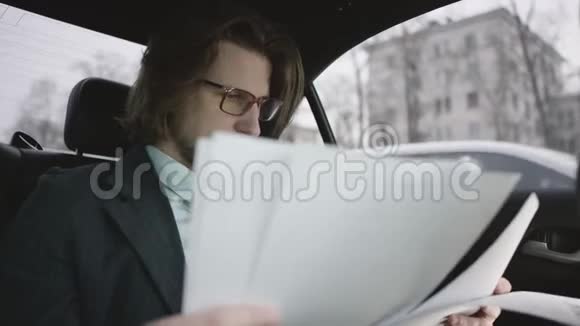 一个英俊的男人棕色头发穿着开心果衬衫灰色西装戴着眼镜坐在车里看文件视频的预览图