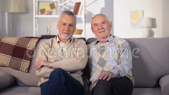 两个老朋友坐在家里的沙发上看着相机社会支持视频的预览图