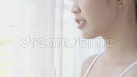 美丽的年轻亚洲女人醒来在家里喝着一杯水窗户是新鲜的视频的预览图