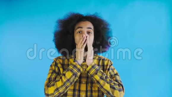 担心的非裔美国人笑着双手盯着她的脸在蓝色背景下庆祝成功视频的预览图
