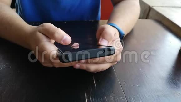 一个穿着蓝色衬衫的男人在触摸屏手机上浏览坐在桌子旁视频的预览图