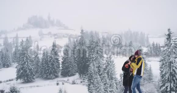 年轻迷人的男人和女人站在田野背景的顶端美丽的雪林他们看着视频的预览图