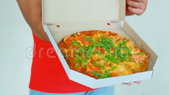 身穿红色制服的英俊年轻送货员正拿着一个披萨看着相机微笑着灰色背景视频的预览图