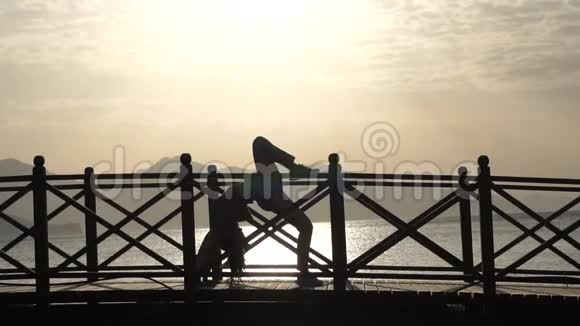 夕阳西下一个女孩站在一座桥上的剪影她的腿在海面上翘起视频的预览图