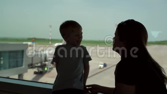 母亲的剪影和儿子站在机场的窗口视频的预览图