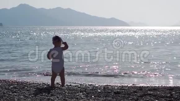 一个婴儿慢吞吞地把一颗鹅卵石从阳光下灿烂的海水里视频的预览图
